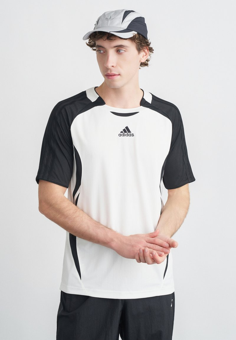 Biała sportowa koszulka z czarnymi akcentami, z krótkimi rękawami i logo Adidas. W komplecie dwukolorowa czapka w odcieniach czerni i szarości.