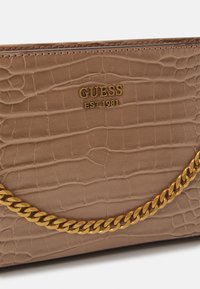 Brun faux læder taske med krokodillemønster, guld "GUESS EST 1981" logo og en guld kædetraspe langs forsiden.