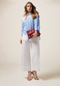 Pantalons larges blancs, chemise rayée bleu et blanc à boutons, pochette rouge avec chaîne, sandales à talons roses, textures lisses, couleurs claires.