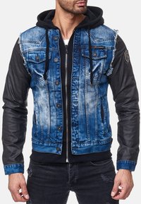 Veste en denim avec un devant bleu délavé, des manches en cuir noir et une capuche, comportant deux poches poitrine et des détails usés.