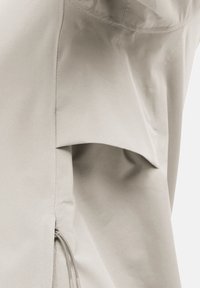 Lichtbeige jas met een gladde textuur, minimalistisch ontwerp en een ritsdetail aan de zijkant. Inclusief een opgestikte zak aan de voorkant.