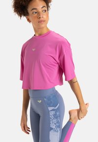 Camiseta atlética corta de color rosa con mangas cortas, combinada con leggings azules que presentan un patrón floral y acentos laterales en contraste de color rosa.