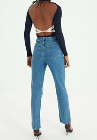 Haut bleu marine à manches longues avec dos ouvert, associé à un jean droit taille haute bleu clair et des talons pointus noirs.