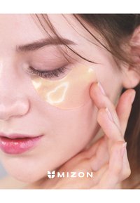 Patch oculaire en hydrogel appliqué sous l'œil ; texture translucide et légèrement brillante ; une personne touche doucement le patch avec le bout des doigts.