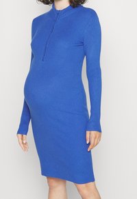 Blå ribbade stickade klänning med hög krage och långa ärmar, som har en framdragkedja och en figurnära siluett. Mjuk textur och elastiskt material.