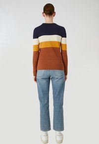 Långärmad stickad topp i marinblått, krämfärgat, gult och rostfärgade ränder. Åtsittande design med ribbad textur. Bärs med ljusblå bootcut-jeans.