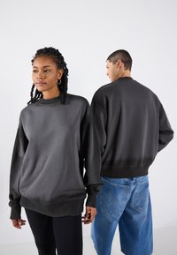Svart crewneck genser med lange ermer, avslappet passform, ribbestrikkede cuffs og hem. Kombinert med denimshorts og ribbestrikkede bukser.