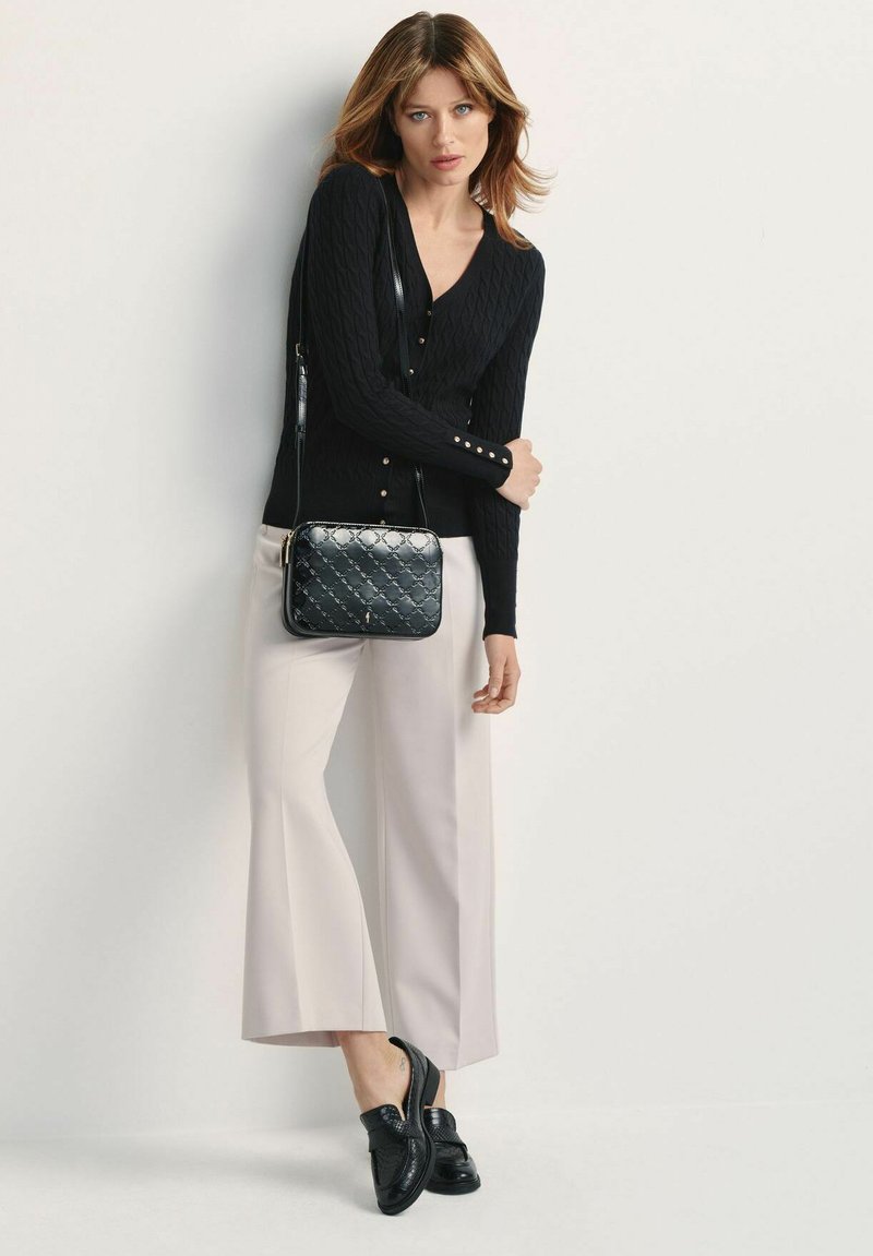 Czarny kardigan w splot sznurkowy z złotymi guzikami, w połączeniu z jasnoszarymi spodniami o szerokich nogawkach i czarnymi loafersami. Czarńska lakierowana torba na ramię dopełnia stylizację.