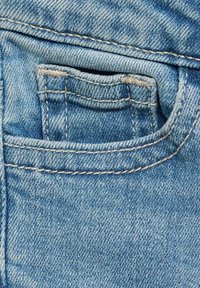 Kratak prikaz denim tkanine u svijetloplavoj nijansi s vidljivim šavovima, ističući rub džepa i teksturiranu površinu.