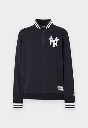 Granatowa bluza z suwakiem do połowy wysokości, z białym logo na piersi, paskowanym kołnierzem i mankietami, miękkim materiałem, o regularnym kroju oraz z etykietą z logo przy dolnym brzegu.