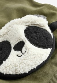 Grønne stoffer med et stort pandaansigt design i bløde hvide og sorte teksturer, der har runde sorte øjne og en broderet næse detalje.