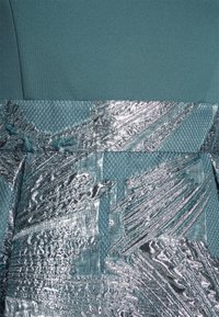 Une robe en tissu teal avec un bas argenté métallique texturé. Le haut est lisse, tandis que le bas présente des motifs abstraits audacieux et une accent en maille.