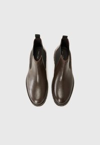 Botines de cuero marrón con un acabado suave, paneles laterales elásticos y tiradores para facilitar su uso. Punta redonda y suelas de goma planas.