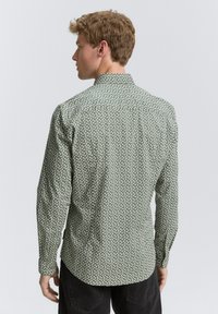 Chemise à manches longues à boutons en coton vert clair avec un motif abstrait blanc, présentant un col standard et des poignets à boutons.