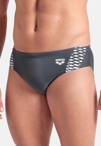 Bañador gris de corte ajustado con una textura suave, que presenta un patrón geométrico blanco en un lado y un logo de "arena" en la parte delantera.