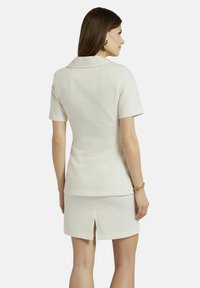 Korteke mouw, crèmekleurig top met een kraag, gecombineerd met een bijpassende rok met een rugsplit. Gladde textuur en getailleerde pasvorm.