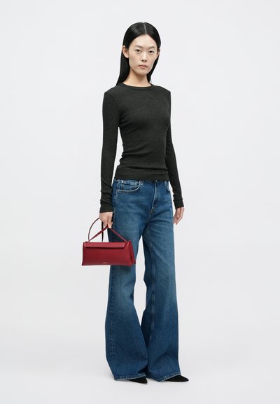 Μαύρο ριμπ μακρυμάνικο πουκάμισο συνδυασμένο με μπλε τζιν παντελόνι με φαρδιά μπατζάκια και ψηλή μέση. Το μοντέλο κρατά μια μικρή κόκκινη δερμάτινη τσάντα χειρός με πάνω λαβή.