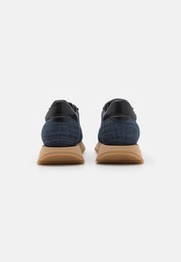 Teniske iz denim tkanine temno modre barve, s črnimi usnjenimi detajli in bež gumijastimi podplati. Zadaj so vidne zaobljene oblike pete in tekstura.