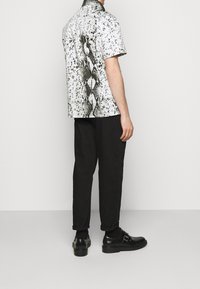 Camicia a maniche corte con motivo in pelle di serpente bianco e nero, realizzata in tessuto leggero. Abbinata a pantaloni neri e scarpe.