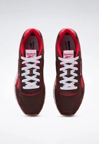 Braune Wildledersneaker mit roten Akzenten und weißen Schnürsenkeln. Verfügt über einen gepolsterten Knöchelbereich und eine Gummisohle. Reebok-Logo auf der Zunge sichtbar.