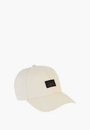 Beige kasket med en buet skygge, fremstillet af blødt stof. Har et sort mærke med hvid tekst på forsiden.