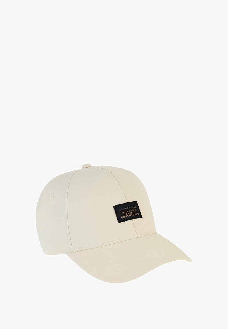 Beżowa czapka z zakrzywionym daszkiem, wykonana z miękkiego materiału. Posiada czarną metkę z białym napisem z przodu.
