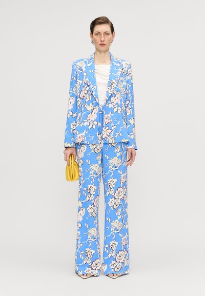Blå blomsterblazer og matchende bukser med store hvide og pink roser, parret med en gul taske. Glat stof, viddebenet pasform.