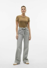 Camiseta ajustada marrón combinada con pantalones de tiro alto, de pierna ancha y color beige con cordones. Textura de tela suave y detalles de costura sutiles.
