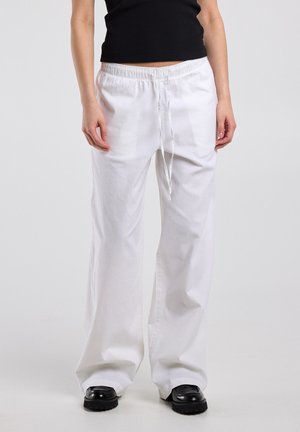 Person wearing loose white drawstring pants, black cropped top, and black chunky-soled shoes standing against a plain background.