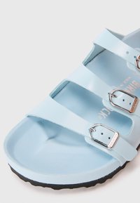 Svijetloplavi Birkenstock sandal s tri podesive srebrne kopče i oblikovanim uloškom na bijeloj pozadini.