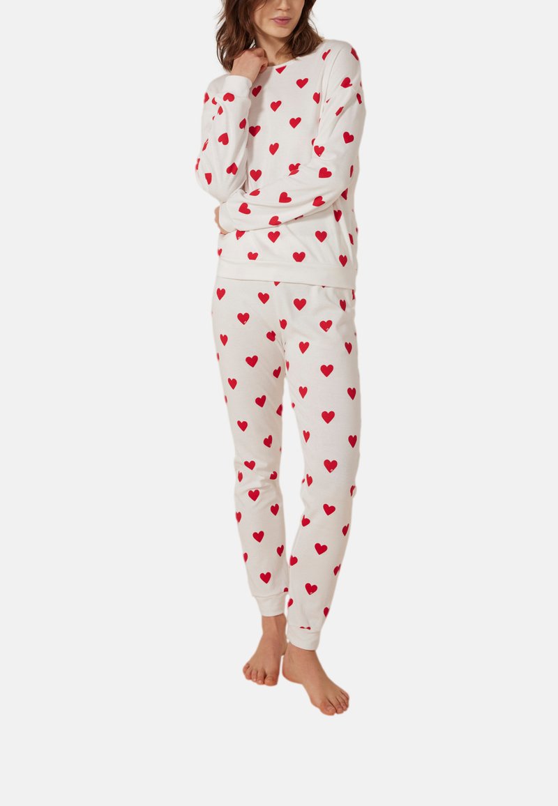 Wit pyjamastel met lange mouwen en broek, voorzien van rode hartpatronen. Gemaakt van zachte stof, met een ontspannen pasvorm en afgeknipte mouwen.