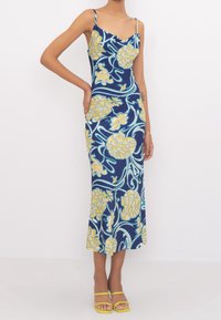 Robe midi marine avec des motifs floraux jaunes et turquoise, des bretelles spaghetti, une silhouette ajustée et une texture de tissu lisse.
