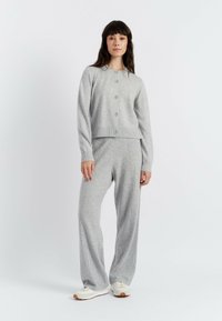 Cardigan grigio a maglia con scollo a girocollo e cinque bottoni, abbinato a pantaloni larghi grigi con cuciture laterali.