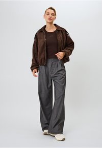 Ruda suede zip-up striukė su prigludusiu ruduo viršumi, derinama su pilkai languotais aukštai juosmeniu keliais ir baltais sportbačiais. Lygus, laisvas jotis.