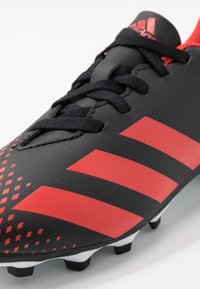 Svart fotbollssko med röda detaljer och tre karakteristiska ränder. Texturerad yta med snörning och formade vita och svarta dobbar.