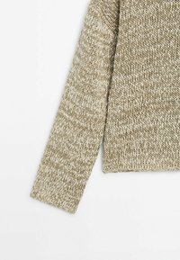 Pull beige en maille avec une coupe ample, des manches longues et un motif texturé. Le tissu semble doux et décontracté.