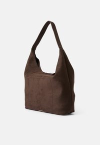 Sac hobo en daim marron avec une large bandoulière douce, présentant une poche avant et un design minimaliste. Texture lisse, sans embellissements.