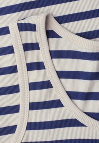 Gros plan d’un tissu côtelé avec des rayures horizontales blanches et bleu marine et une bordure blanche au niveau de l’encolure et de l’emmanchure.