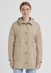 Beige Kapuzenjacke mit Knopfverschlüssen, zwei frontalen Taschen und kontrastierenden Kordeln; glatte Textur mit lockerer Passform.