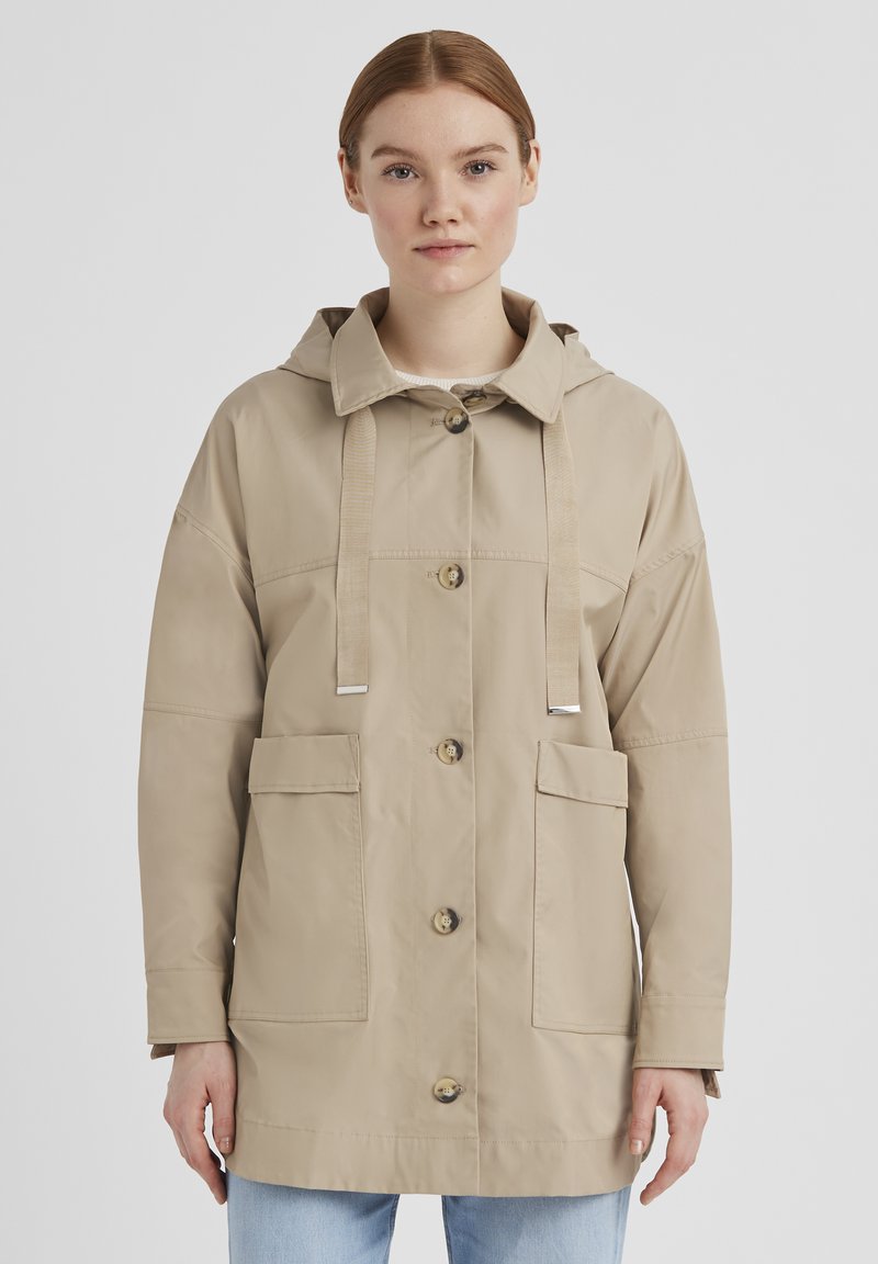 Beige Kapuzenjacke mit Knopfverschlüssen, zwei frontalen Taschen und kontrastierenden Kordeln; glatte Textur mit lockerer Passform.