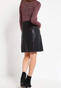 Musta nahkainen A-linjainen hame, jossa on sileä pinta ja puolipitkä malli, yhdistettyinä marooniväriseen teksturoituun neuleeseen ja mustiin nilkkabootseihin.