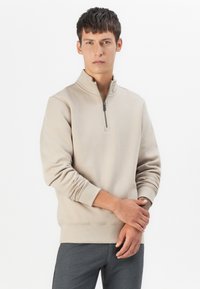 Beige half-zip sweatshirt made from soft fabric, featuring a stand-up collar and ribbed cuffs, styled with a relaxed fit.