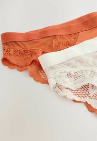 Kaksi naisten alusvaateparia: yksi oranssi pitsireunuksella ja toinen valkoinen vastaavalla pitsikuvioinnilla, molemmissa joustavalla vyötärönauhalla.