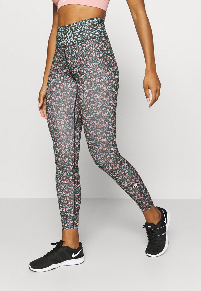 Leggings florales con un fondo negro, que presentan una cintura alta y patrones de flores en tonos rosa brillante y azul. Llevados con zapatillas deportivas negras.