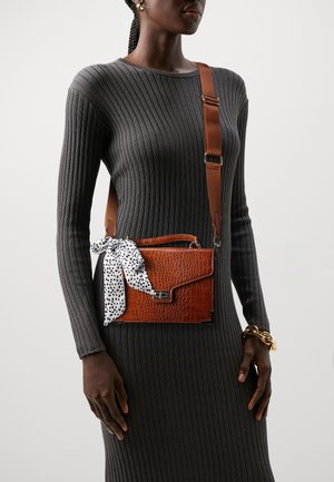 Braune Tasche aus krokodilledergeprägtem Leder mit einer strukturierten Form, einem vorderen Verschluss und einem gepunkteten Schal, der um den Griff gebunden ist. Verstellbarer Riemen.