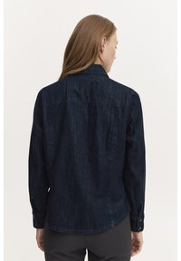 Cămașă din denim închis, cu guler clasic, manșete cu nasturi și croială dreaptă. Designul din spate include coaserea de pe umăr și un singur buzunar pe piept.