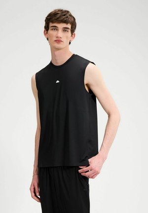 Junger Mann mit kurzen braunen Haaren, der ein ärmelloses schwarzes Sportoberteil und passende schwarze Shorts vor weißem Hintergrund trägt.