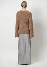 Bruine fluffy trui met lange mouwen, gecombineerd met een gladde, zilveren, vloerlange rok met een textuur.