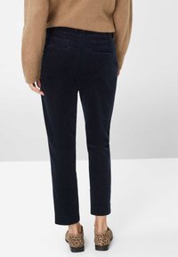 Navy corduroy broeken met een rechte snit, voorzien van achterzakken, gedragen met schoenen met dierenprint. De textuur van de stof voegt visuele interesse toe.