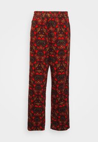 Mönstrade byxor med elastisk midja som har en blandning av röda, orange och bruna blommönster, med en strukturerad textilestetik.